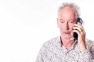 A mature man appears engaged in a serious phone conversation, his expression one of focused contemplation, against a minimalist white background. Senior Man in Thoughtful Conversation Over the Phone