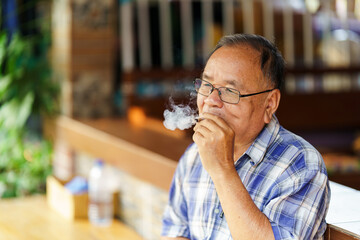 An elderly man was smoking tobacco that was emitting smoke. The concept of harming health.