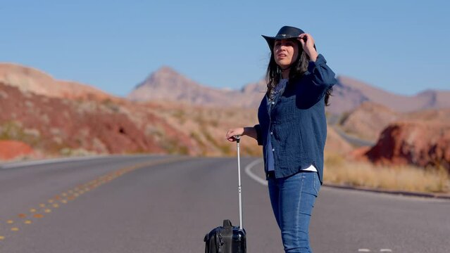 Young woman walking alone through the desert with a suitcase as luggage - travel photography