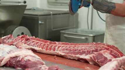 Butcher cutting through pig ribs with automated saw for ribeye steak