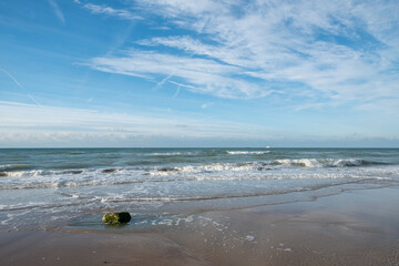 This inviting image showcases a broad view of a sandy beach under a vast blue sky streaked with...
