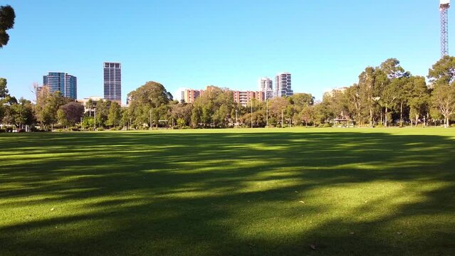 Morning sunlight and shade from trees on football oval and city buildings in background Wellington Square, East Perth