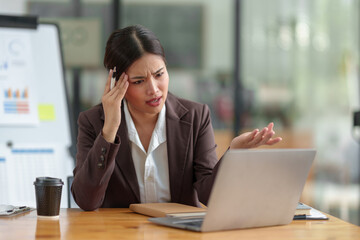 Asian businesswoman who is tired has a headache, is stressed, sleepy, angry, and bored from sitting at a desk for a long time doing contact work. online business on laptop Office syndrome concept.