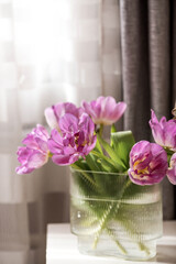 A bouquet of pink tulips in a beautiful stylish vase on the table in the room. The concept of the onset of spring and International Women's Day on March 8.