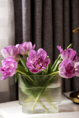A bouquet of pink tulips in a beautiful stylish vase on the table in the room. The concept of the onset of spring and International Women's Day on March 8.