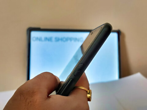 Picture of a person working on a cellphone with ONLINE SHOPPING written on a placard in blur background