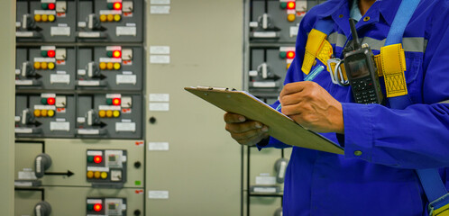 A man is writing on a clipboard in front of a power station