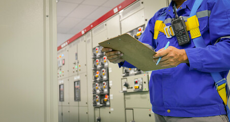 A man in a blue jacket is writing on a clipboard in front of a row of electrical