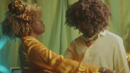 Young happy Black couple dancing and singing on retro theme party in studio with vintage interior and warm light