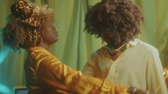 Young happy Black couple dancing and singing on retro theme party in studio with vintage interior and warm light