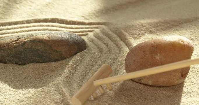 Close-up making zen garden with sand and stones using mini bamboo wooden rake