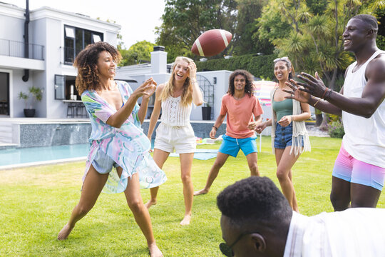 Diverse group of friends enjoy a game of football in a sunny backyard - Powered by Adobe