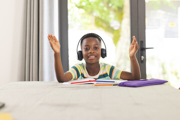African American boy with headphones gestures during an online class