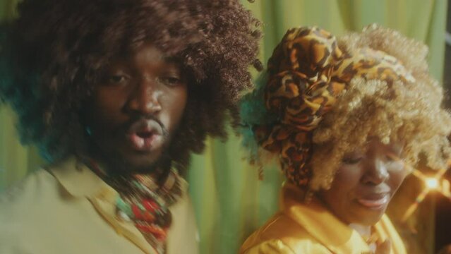 Young handsome African-American man and pretty woman with curly hair smiling at camera and dancing together on a party in retro studio