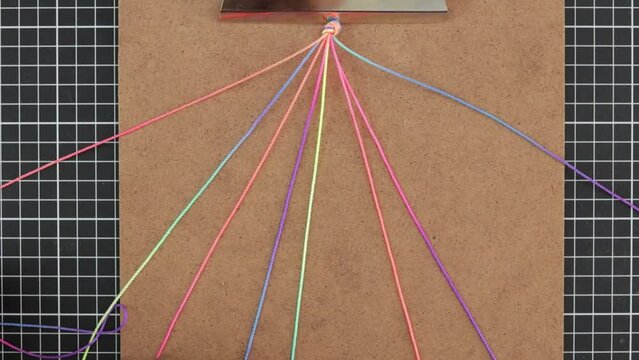 hands weave a colorful rainbow macrame bracelet using multiple vibrant strands