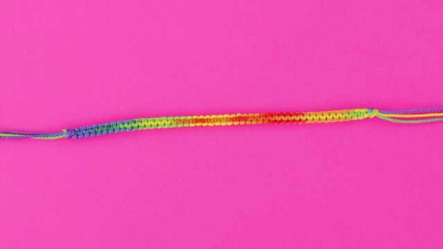 vibrant close-up on threaded macrame bracelet, rainbow pattern set on pink background