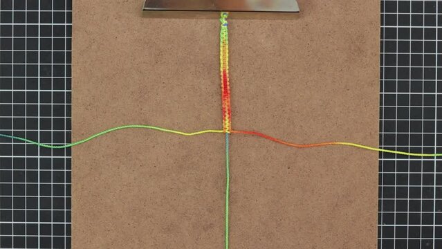Using tweezers to craft vibrant macrame bracelets, with rainbow color threads.