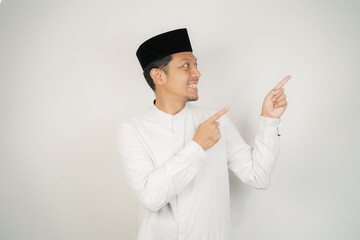 Cheerful handsome Asian Muslim man wearing Arab costume pointing hand finger at empty space for advertising on isolated background