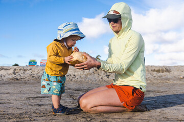 A young boy sips coconut water from a coconut on the beach.