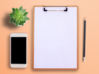 Top view with blank clipboard, smartphone, pot plant and pencil on orange background.