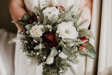 bride holding winter wedding bouquet with white and red flowers