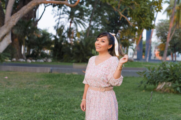 Fototapeta premium Woman with positive attitude wearing dress and bow in her hair in a public park taking a walk.
