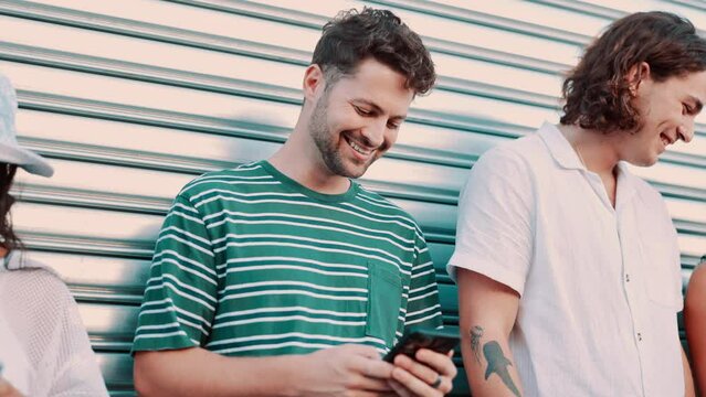 Group, friends and typing with phone in city by garage for contact, blog or connection with diversity. Men, women or gen z people on smartphone, meme and texting for chat, streaming or social media
