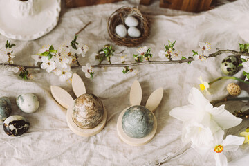 Happy Easter! Stylish easter eggs, bunnies and cherry blossom flat lay on rustic table. Modern natural dyed marble eggs and spring flowers. Easter decor in countryside home