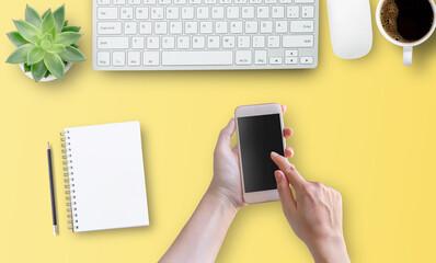 Top view with woman hand using mobile phone with empty screen on yellow table background.
