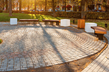 A recreation area in a city park in the form of a round area paved with paving slabs. Along the...