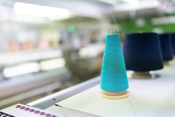 Close-up of blue and black thread rolls on a sewing machine. We are working to prepare to use designers to sew in the large business industry of producing clothing for export to the world market.