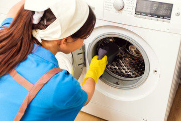 Professional Asian woman cleaning service wearing yellow rubber gloves, using a rag to wipe the washing machine near the kitchen counter at home. Housekeeping cleanup, Woman cleaner concept. - 756226049