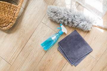 Fototapeta na wymiar Top view of Spray bottle in a side view with blue liquid detergent inside on the wooden floor with rag and grey feather duster in an empty space at home. Spray bottle mockup. Cleaning concept.
