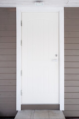 white entrance door on a gray wall of a wooden house with a stone porch and lamp