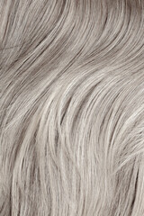 Blond hair close-up as a background. Women's long blonde hair. Beautifully styled wavy shiny curls. Hair coloring. Hairdressing procedures, extension. White hair