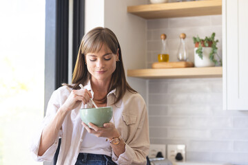Caucasian woman enjoys a meal in a bright kitchen setting