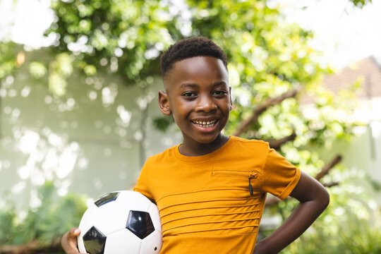 African American boy smiles while holding a soccer ball outdoors in the backyard