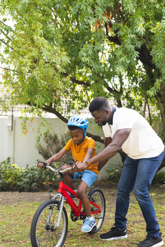 African American father teaches his son to ride a bike in a lush garden