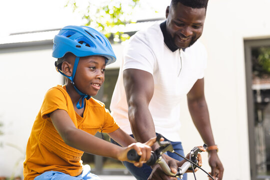 African American father teaches his son to ride a bike in the backyard, both smiling joyfully