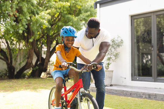 African American father helps his son learn to ride a bike in a sunny backyard