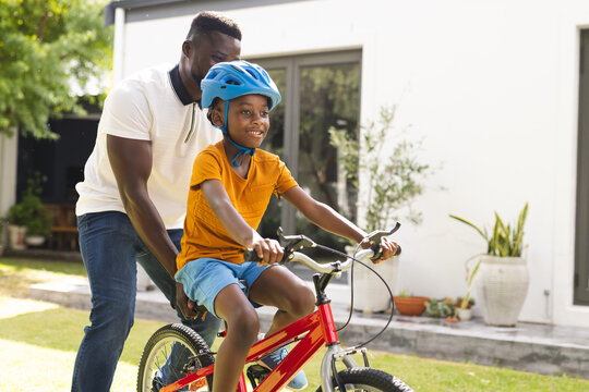 African American father teaches his son to ride a bike in a sunny backyard
