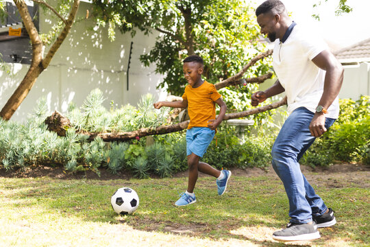 African American father plays soccer with his son in a sunny backyard