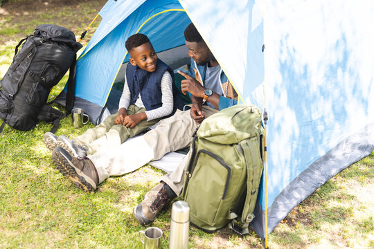 African American father and son enjoy a camping trip, sitting inside a blue tent