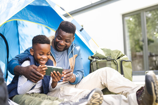 African American father and son share a moment with a smartphone inside a tent in their backyard - Powered by Adobe