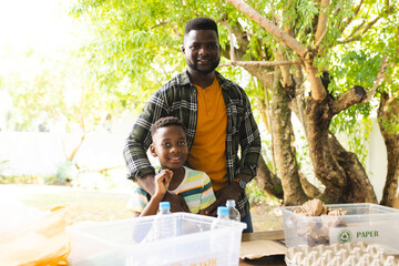 African American father and son smile near recycling bins outdoors