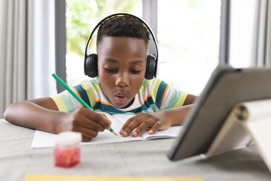 An African American boy engages in drawing online, wearing headphones and focused on a tablet