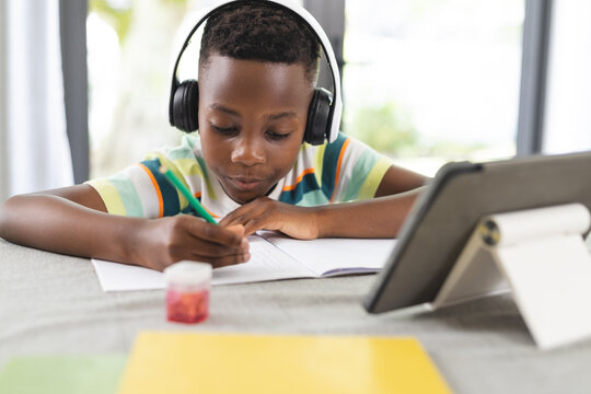 African American boy with headphones focuses on writing in a notebook