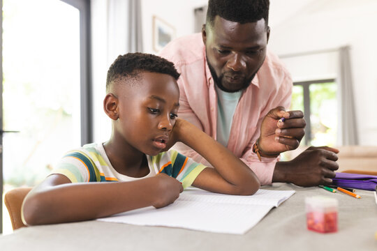 African American father assists a young son with homework at a table