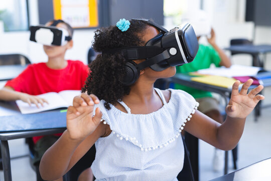 Biracial girl with curly hair uses VR headset in a classroom at school - Powered by Adobe