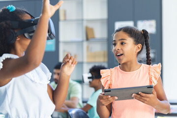 Two biracial girls are engaged in interactive technology play in the classroom at school